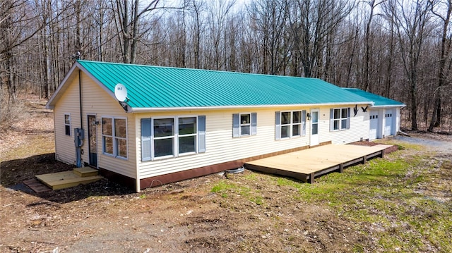 rear view of property featuring metal roof, entry steps, an attached garage, and a wooded view