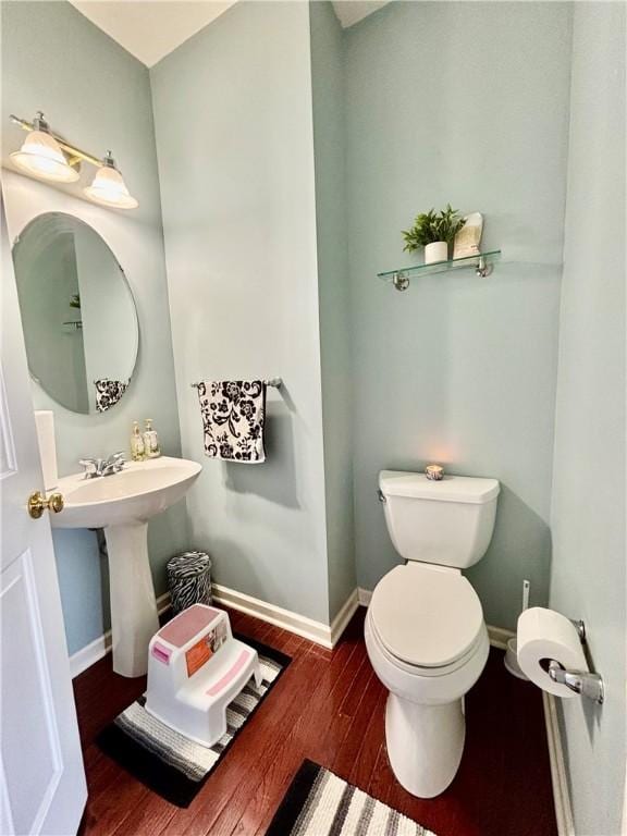 half bathroom featuring baseboards, wood finished floors, and toilet