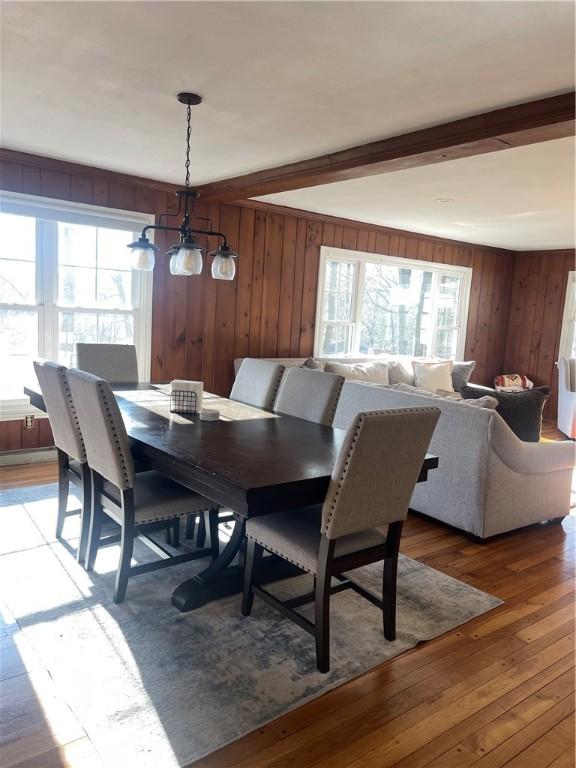 dining room featuring light wood-type flooring, wooden walls, and beam ceiling