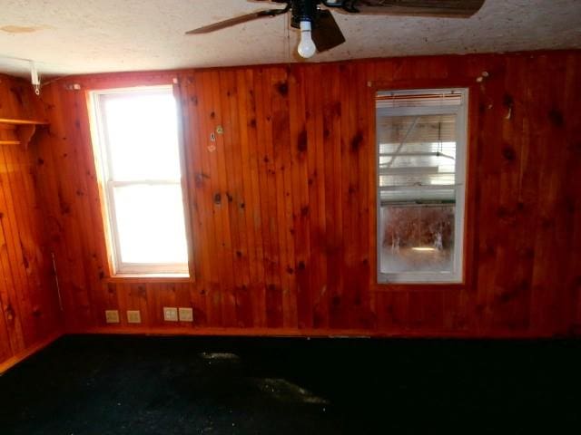 empty room with a textured ceiling, wooden walls, and a ceiling fan