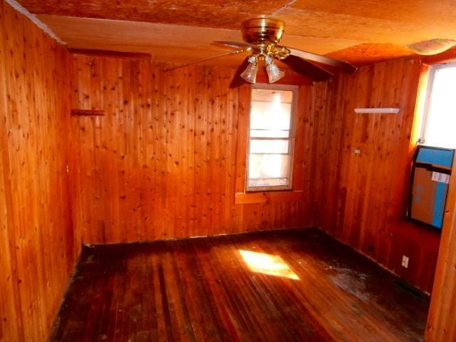 unfurnished room with ceiling fan, wood walls, and hardwood / wood-style floors
