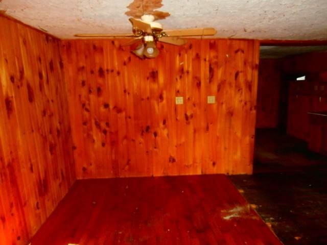 spare room with a textured ceiling, wooden walls, wood finished floors, and a ceiling fan
