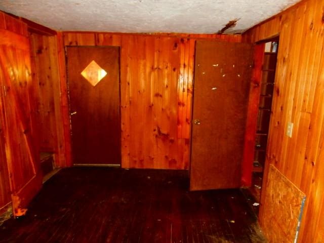 interior space with a textured ceiling, wooden walls, and hardwood / wood-style flooring