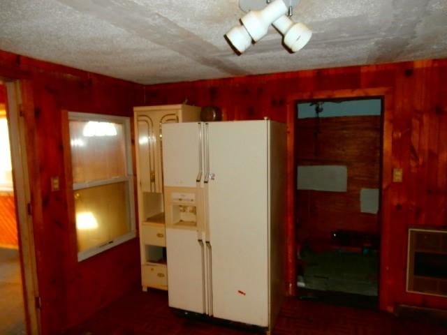 kitchen featuring a textured ceiling, white refrigerator with ice dispenser, and wooden walls