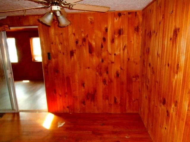 empty room featuring a ceiling fan, wood walls, a textured ceiling, and wood finished floors