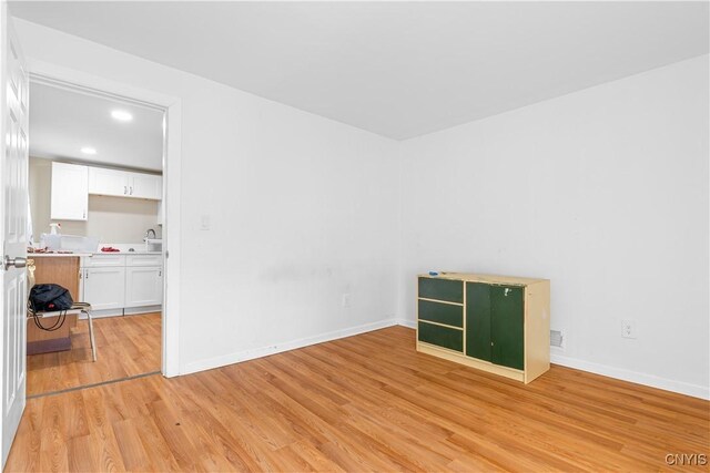 unfurnished room featuring light wood finished floors, baseboards, recessed lighting, and a sink