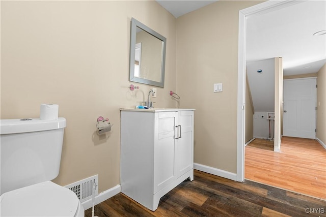 half bath featuring visible vents, baseboards, toilet, wood finished floors, and vanity