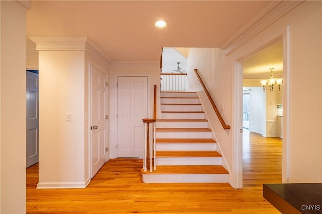 stairs with baseboards, ornamental molding, wood finished floors, recessed lighting, and ceiling fan with notable chandelier