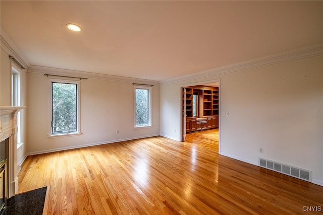 unfurnished room with light wood-type flooring, crown molding, a premium fireplace, and visible vents