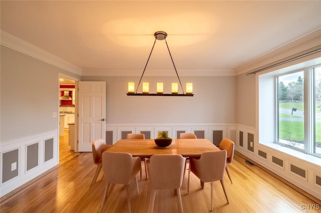 dining area with a wainscoted wall, ornamental molding, light wood-type flooring, and a notable chandelier