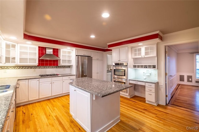 kitchen with a kitchen island, open shelves, appliances with stainless steel finishes, wall chimney range hood, and ornamental molding