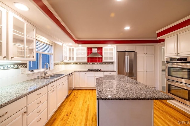 kitchen with decorative backsplash, wall chimney exhaust hood, a kitchen island, appliances with stainless steel finishes, and a sink