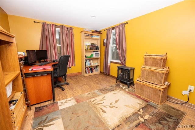 office area with baseboards, wood finished floors, and a wood stove