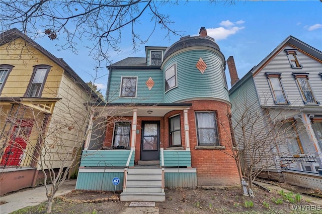victorian house with a porch, brick siding, and a chimney