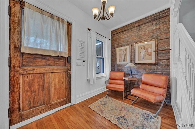 living area with a chandelier, wood finished floors, baseboards, and brick wall