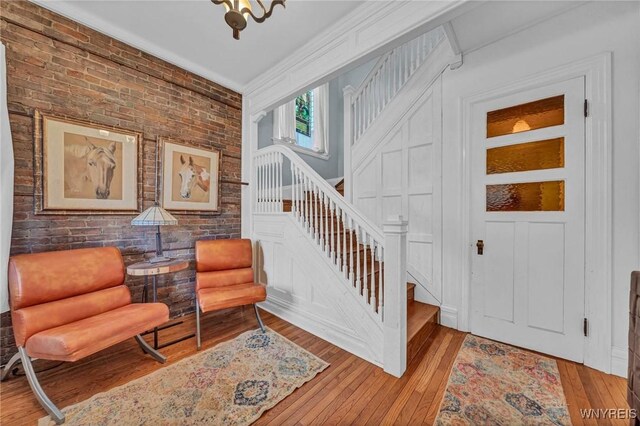 foyer featuring stairway, light wood finished floors, crown molding, and brick wall