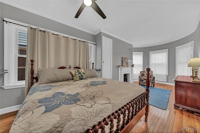 bedroom with wood finished floors, baseboards, a ceiling fan, crown molding, and a fireplace