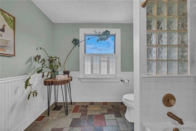full bath featuring wainscoting, stone finish floors, a tub to relax in, toilet, and a shower