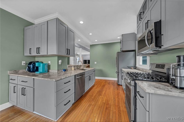 kitchen with appliances with stainless steel finishes, crown molding, baseboards, light wood-style floors, and light stone counters