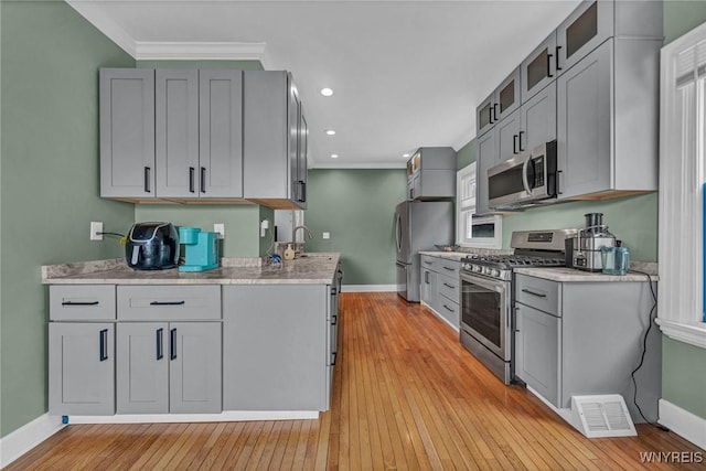 kitchen with stainless steel appliances, baseboards, gray cabinets, a sink, and ornamental molding