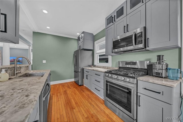 kitchen with appliances with stainless steel finishes, a sink, crown molding, glass insert cabinets, and light wood-style floors