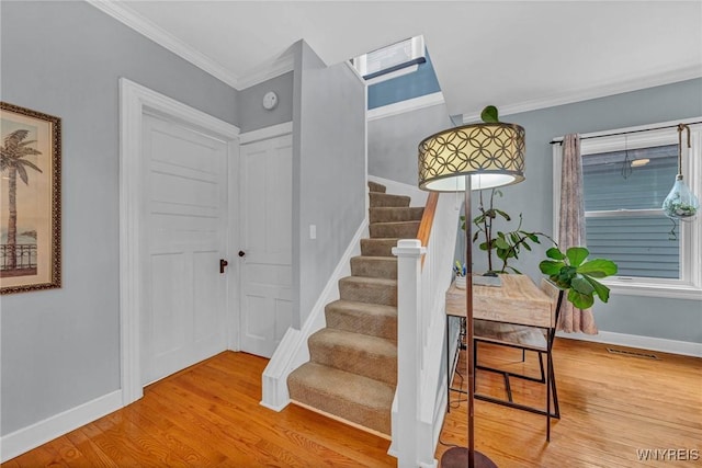 staircase with wood finished floors, ornamental molding, and baseboards