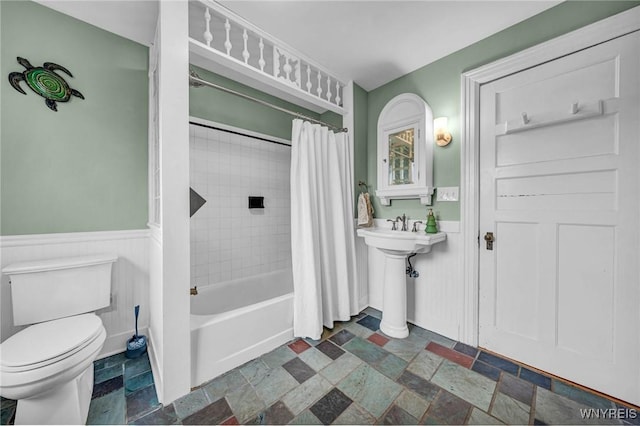 full bathroom with toilet, stone tile floors, wainscoting, shower / bath combo, and a sink