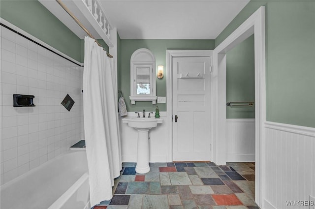 bathroom with shower / bath combo, stone finish flooring, and a wainscoted wall