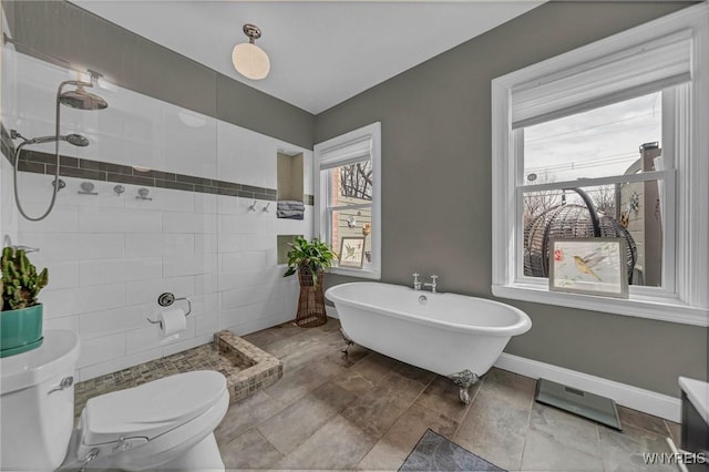 bathroom featuring toilet, a tile shower, a freestanding bath, and baseboards