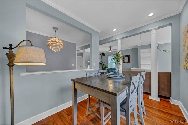 dining room with decorative columns, wood finished floors, baseboards, ceiling fan, and ornamental molding