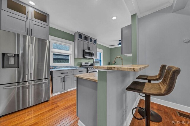 kitchen featuring appliances with stainless steel finishes, ornamental molding, light wood-style flooring, a breakfast bar, and a peninsula