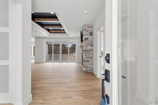 corridor with baseboards, light wood finished floors, and a tray ceiling
