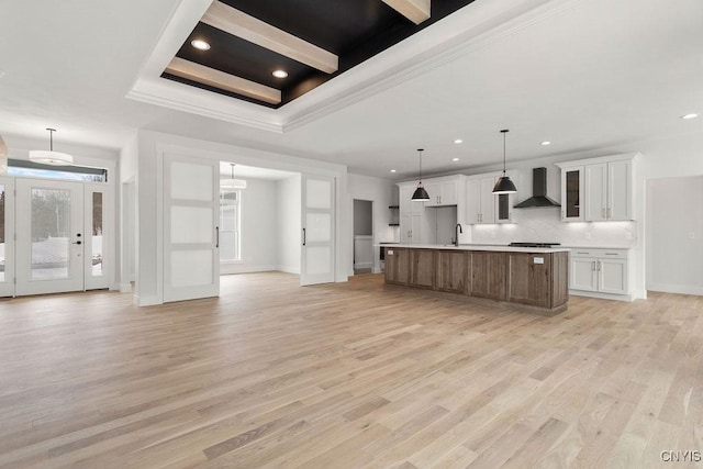 kitchen with light wood-style floors, light countertops, wall chimney exhaust hood, and white cabinetry