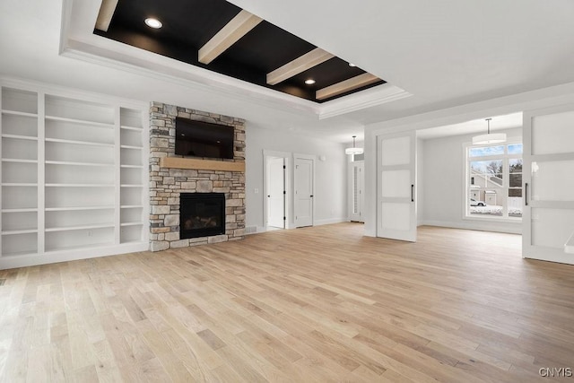 unfurnished living room featuring crown molding, a fireplace, a tray ceiling, and light wood-type flooring
