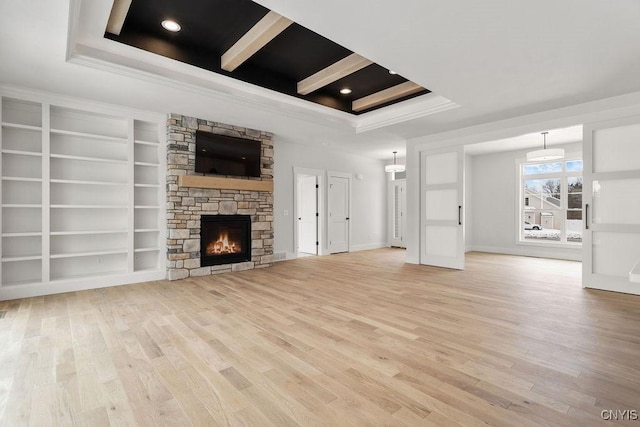 unfurnished living room featuring crown molding, a raised ceiling, light wood finished floors, and a stone fireplace
