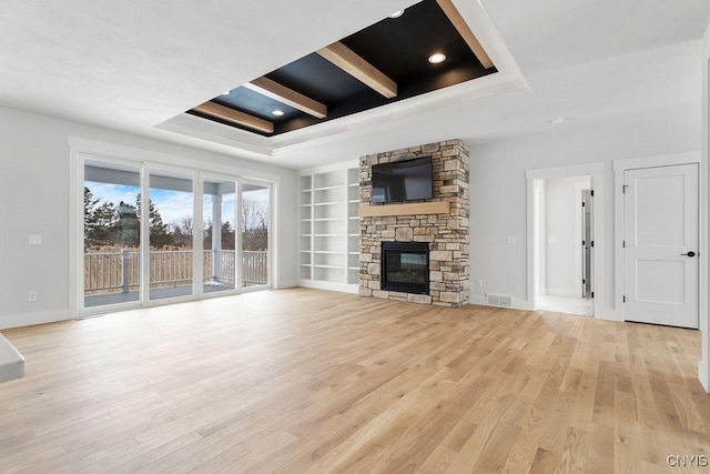 unfurnished living room with built in features, light wood-style flooring, and a tray ceiling