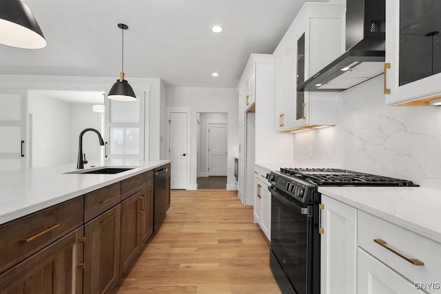 kitchen with a sink, light wood finished floors, wall chimney exhaust hood, white cabinetry, and black appliances
