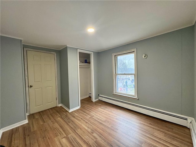 unfurnished bedroom featuring a baseboard radiator, wood finished floors, a closet, and baseboards