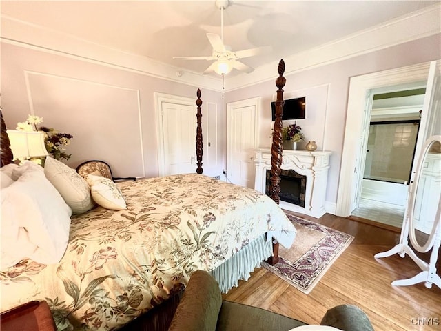 bedroom with a fireplace, ceiling fan, and wood finished floors