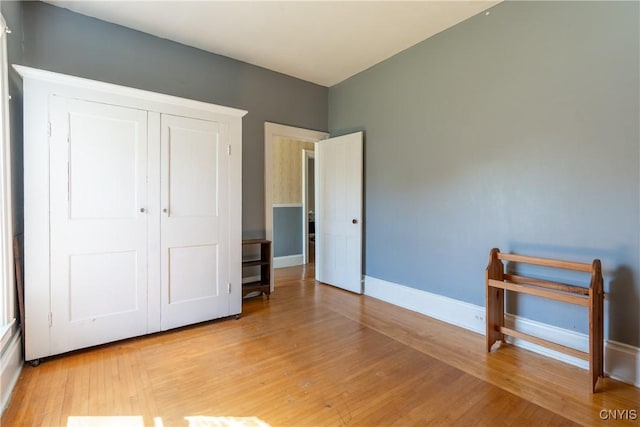 unfurnished bedroom featuring light wood-style flooring, a closet, and baseboards