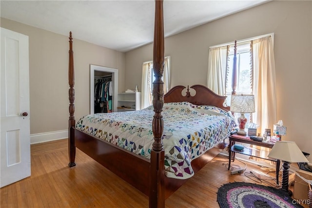 bedroom featuring a spacious closet, baseboards, a closet, and wood finished floors