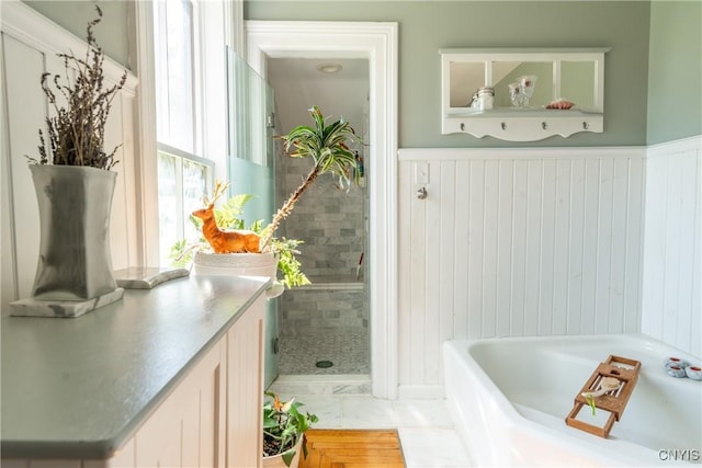 bathroom with a garden tub, vanity, and a wainscoted wall