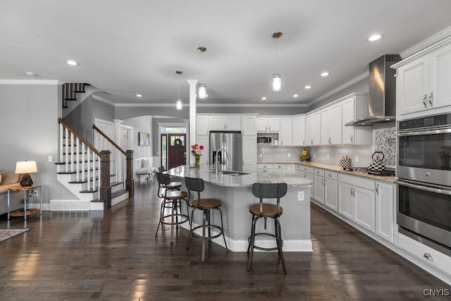 kitchen with wall chimney range hood, dark wood-type flooring, appliances with stainless steel finishes, arched walkways, and a sink