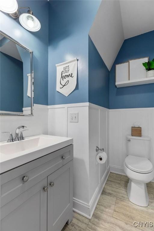 bathroom with vanity, a wainscoted wall, toilet, wood finished floors, and lofted ceiling