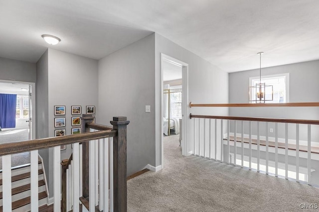 hallway featuring baseboards, an upstairs landing, carpet flooring, and a notable chandelier