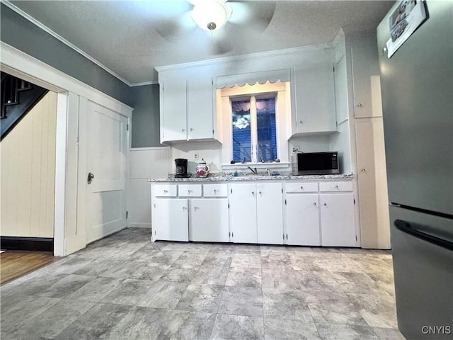 kitchen with a sink, appliances with stainless steel finishes, a textured ceiling, crown molding, and white cabinetry