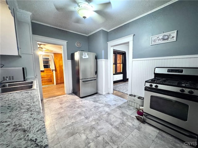 kitchen with ceiling fan, light countertops, a sink, wainscoting, and stainless steel appliances