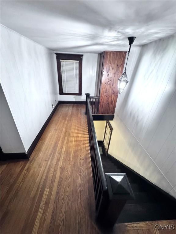 corridor featuring baseboards, dark wood-style floors, and an upstairs landing