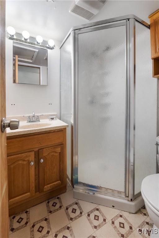 bathroom featuring vanity, a stall shower, tile patterned floors, toilet, and visible vents