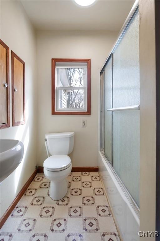bathroom featuring tile patterned floors, toilet, combined bath / shower with glass door, and baseboards